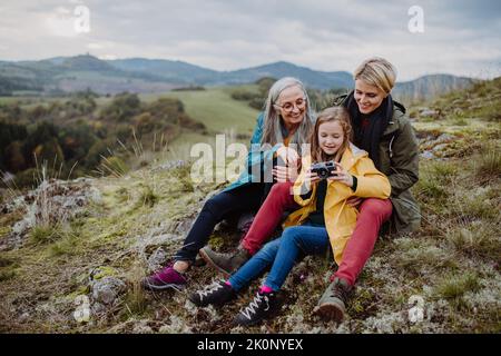 Ältere Frau, die am Herbsttag ihre Tochter und Enkelin auf dem Hügel fotografiert. Stockfoto