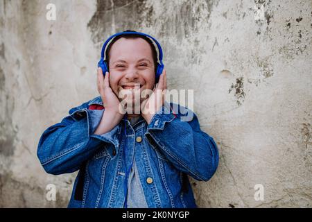 Nahaufnahme eines glücklichen jungen Mannes mit Down Sydrome, der beim Gehen auf der Straße Musik hört. Stockfoto
