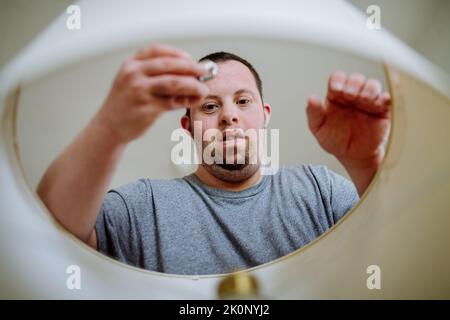 Glücklicher junger Mann mit Down-Syndrom Glühbirne in Innenräumen zu Hause ändern Stockfoto