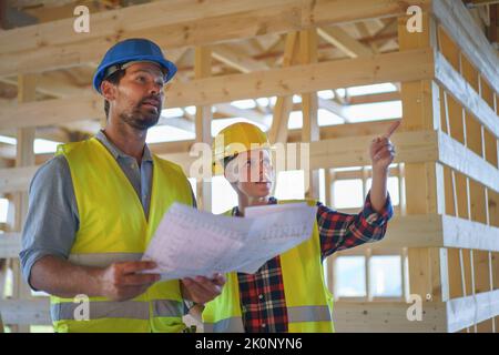 Bauingenieure oder Architekten mit Plänen zur Überprüfung der Öko-Baustelle des Holzrahmenhauses Stockfoto