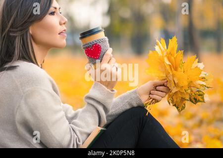 Junge Frau mit gemischter Rasse trinkt Kaffee im Herbstpark Stockfoto