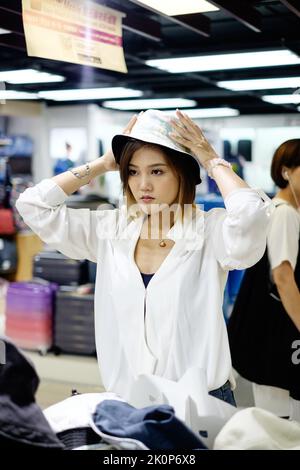 Asiatische Dame probiert einen Hut in einem Geschäft Stockfoto