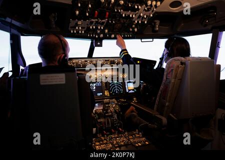 Frau Copilot Unterstützung Kapitän zum Start und Flugzeug fliegen, mit Tasten auf Dashboard-Befehl im Pilot-Cockpit. Airliner fliegen Flugzeug Jet mit Navigations-Windschutzscheibe und Bedienfeld. Stockfoto