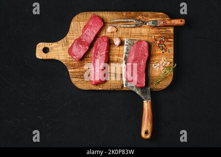 Draufsicht auf rohes, knochenloses Streifensteak auf schwarzem Hintergrund Stockfoto