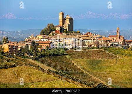 Blick auf die kleine Stadt auf dem Hügel mit bunten herbstlichen Weinbergen im Piemont, Norditalien. Stockfoto