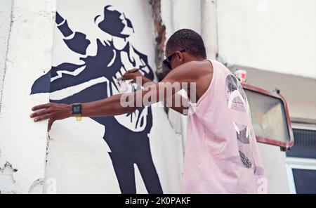 Kreativer Ausdruck. Ein junger Graffiti-Künstler, der ein Design an eine Wand malt. Stockfoto