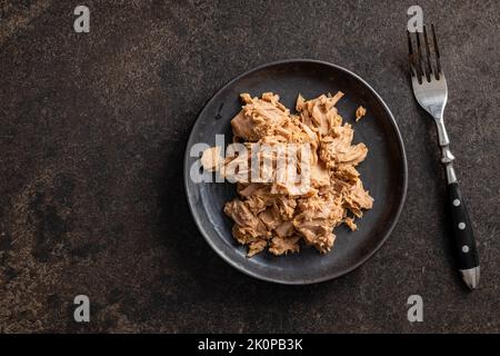 Thunfischkonserven auf dem Teller auf dem schwarzen Tisch. Draufsicht. Stockfoto