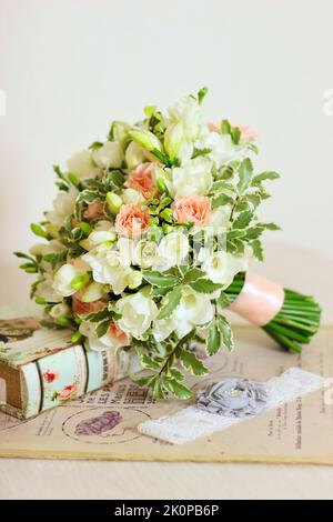 Bouquet von weißen Freesia Blume, rosa Rosen und Blätter und Buch auf hellbeigem Hintergrund. Griff mit pfirsichfarbenem Band. Blumenstrauß, Jahrgang Stockfoto