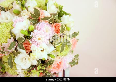 Rundes Bouquet mit weißer Freesia-Blume, grünem Dianthus, Pfirsichrosen, heller Chrysantheme und frischem Grün. Brautstrauß und Holz auf rosa Hintergrund Stockfoto