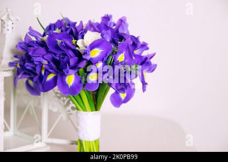 Blumenstrauß aus Iris mit weißen Rosen und weißer dekorativer Laterne auf beigem Hintergrund. Nahaufnahme, Vorderansicht, Kopierbereich. Stockfoto