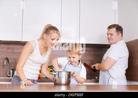 Familie Mutter Sohn, Vater bereiten köstliche Speisen in der Küche. Mama lehrt schönes Kind zu kochen. Glücklich lächelnde Eltern und liebevolles Kind verbringen Zeit zusammen zu Hause. Kochen gesunde Lebensmittel und Abendessen Stockfoto