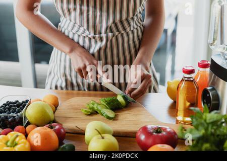 Nahaufnahme von Hausfrau Frau, Mädchen Hände schneiden Gurke in der Küche auf Schneidebrett. Frau macht einen gesunden kalorienarmen Salat, bereiten grünen Detox Shake oder Smoothie für die Ernährung zu Hause. Stockfoto