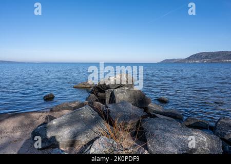 Felsbrocken als Teil eines Wellenbrechers in einem See. Bild vom See Vattern, Schweden. Blaues Wasser und Himmel im Hintergrund Stockfoto