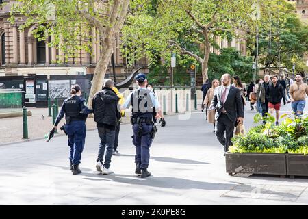 Die australische NSW-Polizei in Sydney eskortiert einen festhafteten Mann entlang der George Street in Sydney, einen bewaffneten und uniformierten Polizeibeamten in Sydney Stockfoto