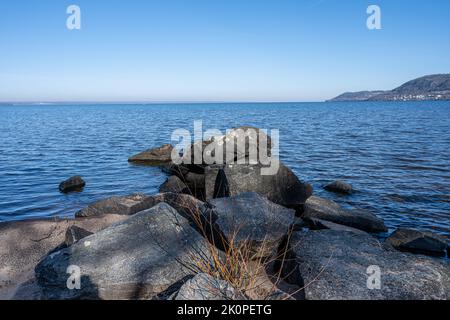 Felsbrocken als Teil eines Wellenbrechers in einem See. Bild vom See Vattern, Schweden. Blaues Wasser und Himmel im Hintergrund Stockfoto