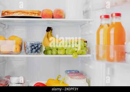 Vorderansicht der offenen, zweitürigen Kühl- oder Kühlschranktür, gefüllt mit frischem Obst, Gemüse, Saft, voller gesunder Lebensmittel und Zutaten im Inneren. Elektrische Küche und Haushaltsgeräte Stockfoto