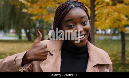 Lächelnde, glückliche junge afroamerikanische Frau, die die Kamera anschaut und den Daumen nach oben zeigt, wenn sie eine Serviceempfehlung gibt, positives Feedback gibt, fühlt sich zufrieden Stockfoto