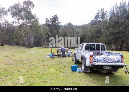 Mann, der auf einem australischen Campingplatz in New South Wales kocht, wobei das Mazda ute-Fahrzeug neben der Lagerküche in NSW, Australien, geparkt ist Stockfoto