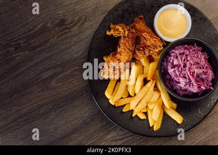 Gebratene, gebratene, panierte Hähnchenfleischstreifen mit Rübenwurzelsalat, pommes auf Holztisch im Café. Draufsicht, Kopierbereich Stockfoto