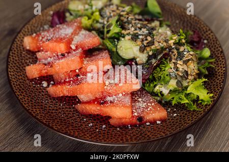 Nahaufnahme in Scheiben geschnittene Wassermelone mit Zuckerpulver oder Salz und Gemüse, Gurken, Auberginen-Salat auf dem Teller. Diät essen Stockfoto