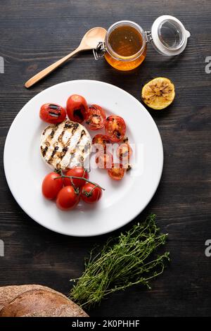 Der Camembert-Käse ist rund, gegrillt, mit goldenem Honig auf einem hölzernen Schneidebrett gegossen. Weicher selektiver Fokus, schwarzer Hintergrund.Platz zum Kopieren. Gesunde Ernährung. Vertikales Foto. Stockfoto