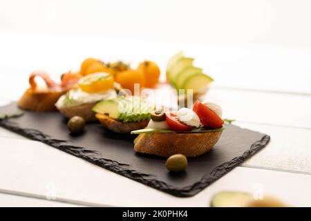 Leckere Snacks, Sandwiches, Crostini, Canape, Antipasti mit Lachs Avocado, Tomaten, Frischkäse, Mozzarella für Party, Geburtstag. Das Konzept der gesunden Ernährung und der mediterranen Küche. Stockfoto