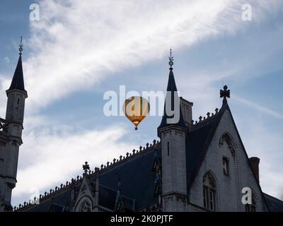 Ein farbenfroher Heißluftballon fliegt über das neugotische Rathaus der Stadt Sint Niklaas in Belgien Stockfoto