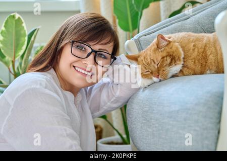 Porträt einer lächelnden Frau mit einer Katze, die auf einem Sessel zu Hause liegt Stockfoto