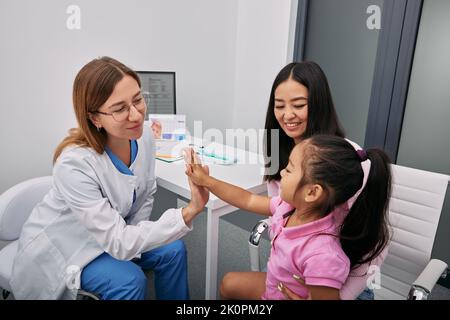 Freundliche Kinderärztin, die sich im Krankenhaus mit asiatischer Mutter und Kind trifft. Beratung, Gesundheit von Kindern Stockfoto