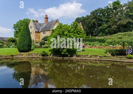 Ein Sommerblick über den Ziersee zum Herrenhaus, Coton Manor Gardens, in der Nähe von Guilsborough, Northamptonshire, Großbritannien Stockfoto