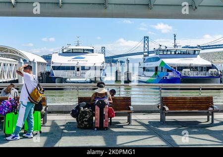 Zwei San Francisco Bay Ferries, die im San Francisco Ferry Terminal festgemacht sind. Passagiere sitzen und warten auf Holzbänken. Stockfoto