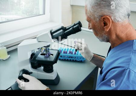 Laborant untersucht Blutproben mit einem medizinisch-wissenschaftlichen Mikroskop im Krankenhauslabor Stockfoto
