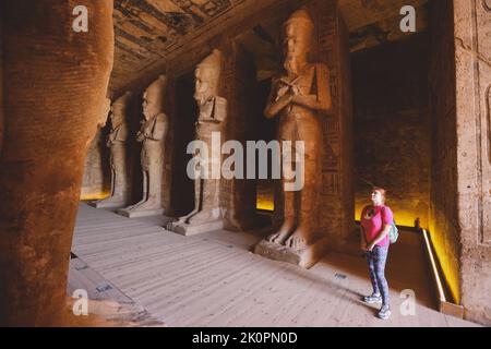 Weißer Tourist vor den kolossalen Statuen von Ramesses II sitzend auf einem Thron nahe dem Eingang zum Großen Tempel in Abu Simbel, Ägypten Stockfoto
