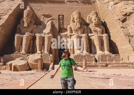 Weißer Tourist vor den kolossalen Statuen von Ramesses II sitzend auf einem Thron nahe dem Eingang zum Großen Tempel in Abu Simbel, Ägypten Stockfoto