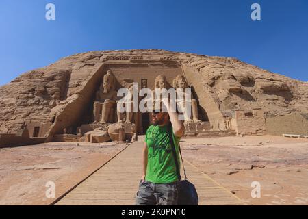 Weißer Tourist vor den kolossalen Statuen von Ramesses II sitzend auf einem Thron nahe dem Eingang zum Großen Tempel in Abu Simbel, Ägypten Stockfoto