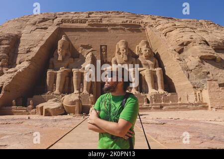 Weißer Tourist vor den kolossalen Statuen von Ramesses II sitzend auf einem Thron nahe dem Eingang zum Großen Tempel in Abu Simbel, Ägypten Stockfoto