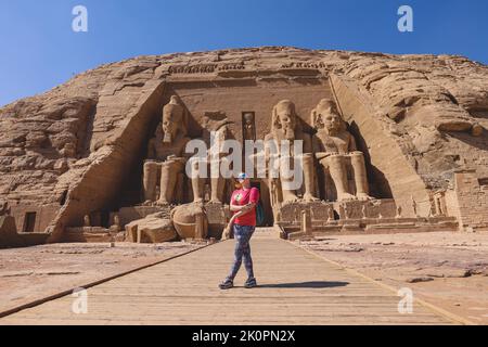 Weißer Tourist vor den kolossalen Statuen von Ramesses II sitzend auf einem Thron nahe dem Eingang zum Großen Tempel in Abu Simbel, Ägypten Stockfoto