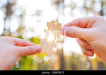 Crop-Ansicht der Hände versuchen, Holz-Puzzles gegen einen Bokeh Wald Hintergrund mit Sonnenlicht durch kommen. Kreativer Seelenverwandter concep Stockfoto