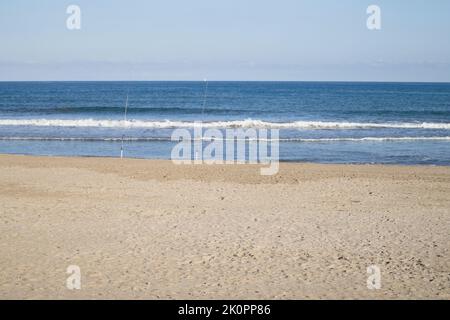 Landschaft mit Blick auf das Meer an einem Tag von leichtem Wind, der einige sanfte Wellen aufwirft und an dessen Strand einige Fischer ihre Angelruten verlassen haben Stockfoto