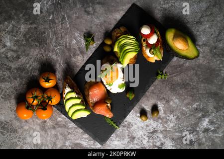 Leckere Snacks, Sandwiches, Crostini, Canape, Antipasti mit Lachs Avocado, Tomaten, Frischkäse, Mozzarella für Party, Geburtstag. Das Konzept der gesunden Ernährung und der mediterranen Küche. Stockfoto