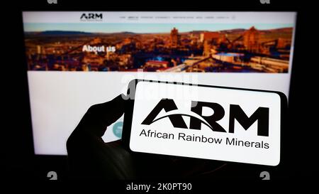 Person mit Mobiltelefon und Logo der Firma African Rainbow Minerals Limited (ARM) auf dem Bildschirm vor der Webseite. Konzentrieren Sie sich auf die Telefonanzeige. Stockfoto