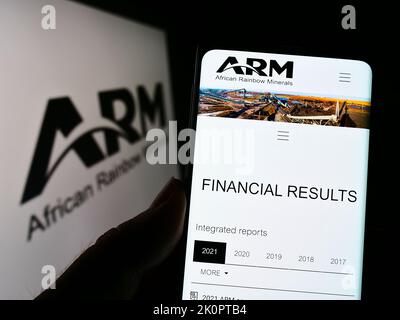 Person, die Mobiltelefon mit der Webseite der Firma African Rainbow Minerals Limited (ARM) auf dem Bildschirm mit Logo hält. Konzentrieren Sie sich auf die Mitte des Telefondisplays. Stockfoto