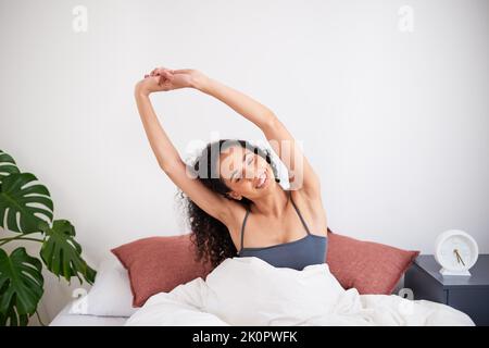 Eine junge, multiethnische Frau streckt sich im Bett und wacht morgens auf Stockfoto