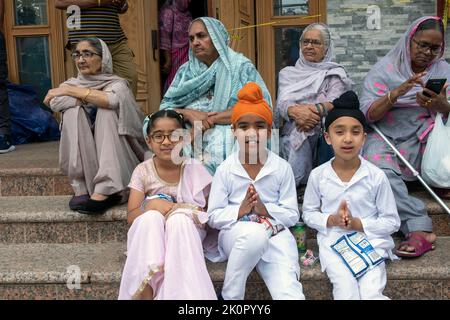 Auf den Stufen des Sikh Cultural Center warten Kinder und Senioren auf den Beginn der Nagar Kirtan Parade. In Richmond Hill, Queens, NYC Stockfoto