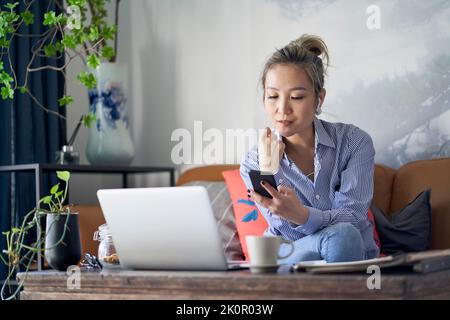 Professionelle asiatische Geschäftsfrau arbeitet von zu Hause aus Video-Chat mit Handy und Laptop-Computer Stockfoto