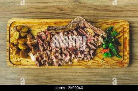 Saftiges und appetitliches Rinderfleischsteak mit Kartoffeln und Padron-Paprika. Spanisches Chuleton de Ternera. Gegrilltes Fleisch an Holzschneidebrett. Obere V Stockfoto