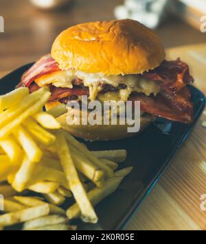 Leckerer Hamburger mit knusprigem Speck, geschmolzenem Käse und pommes auf dem Holztisch Stockfoto