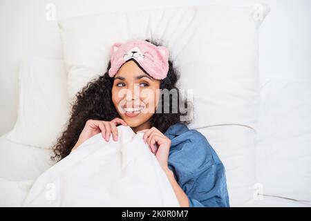 Eine junge multiethnische Frau wacht im Bett mit einer niedlichen Kätzchen-Schlafmaske auf Stockfoto