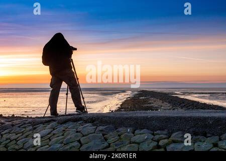 Tourist mit Kamera bei Sonnenuntergang auf Trischedamm, Nordsee bei Ebbe Stockfoto