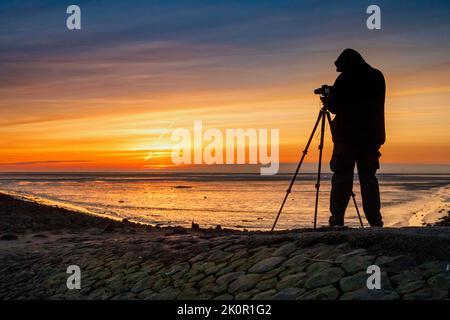 Tourist mit Kamera bei Sonnenuntergang auf Trischedamm, Nordsee bei Ebbe Stockfoto